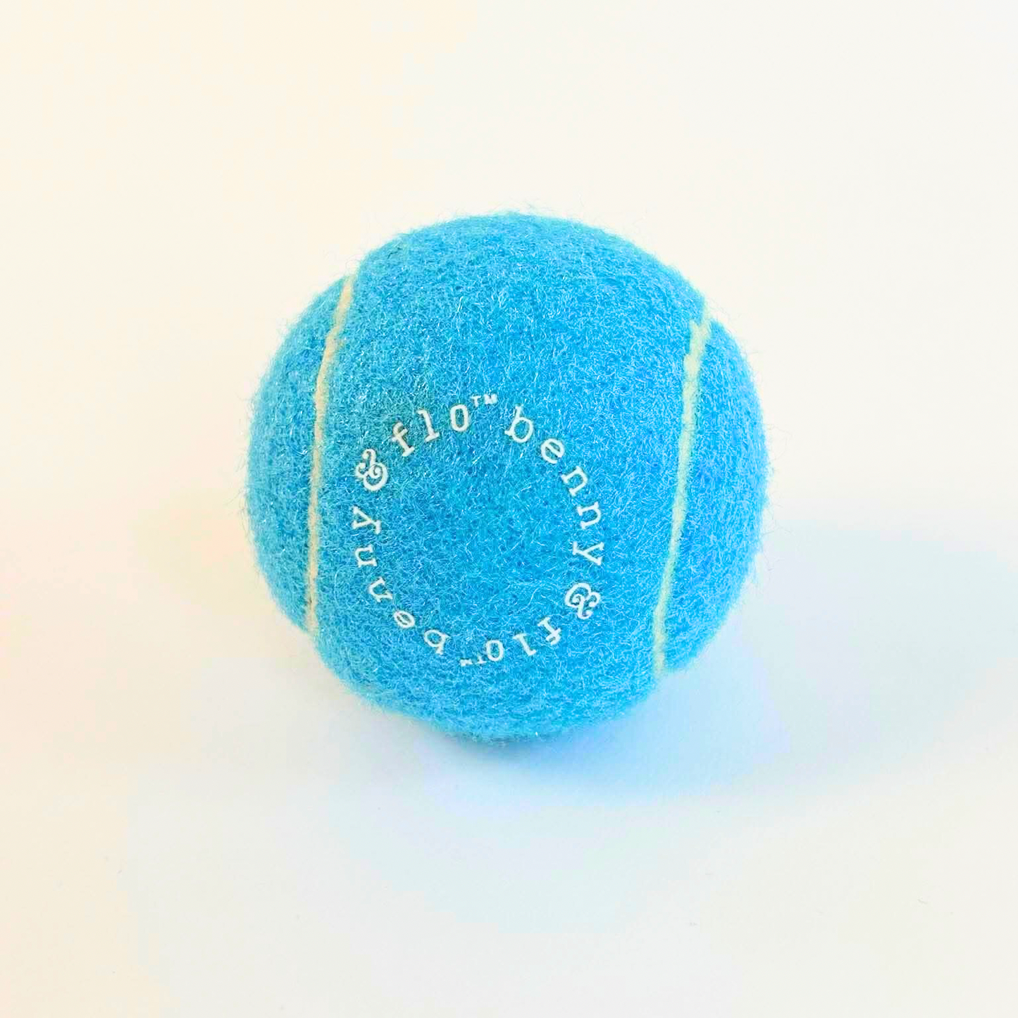 Blue tennis ball with 'benny & Flo’ branding on a light background