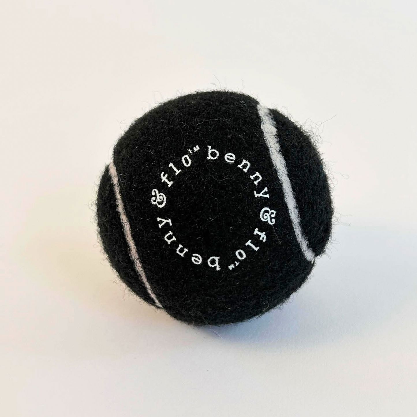 Black branded benny & Flo tennis ball with white text on a light background