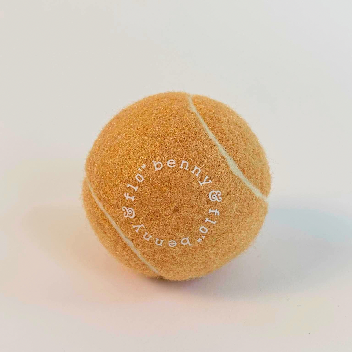 Nude tennis ball with 'Benny & Flo ' branding on a light background