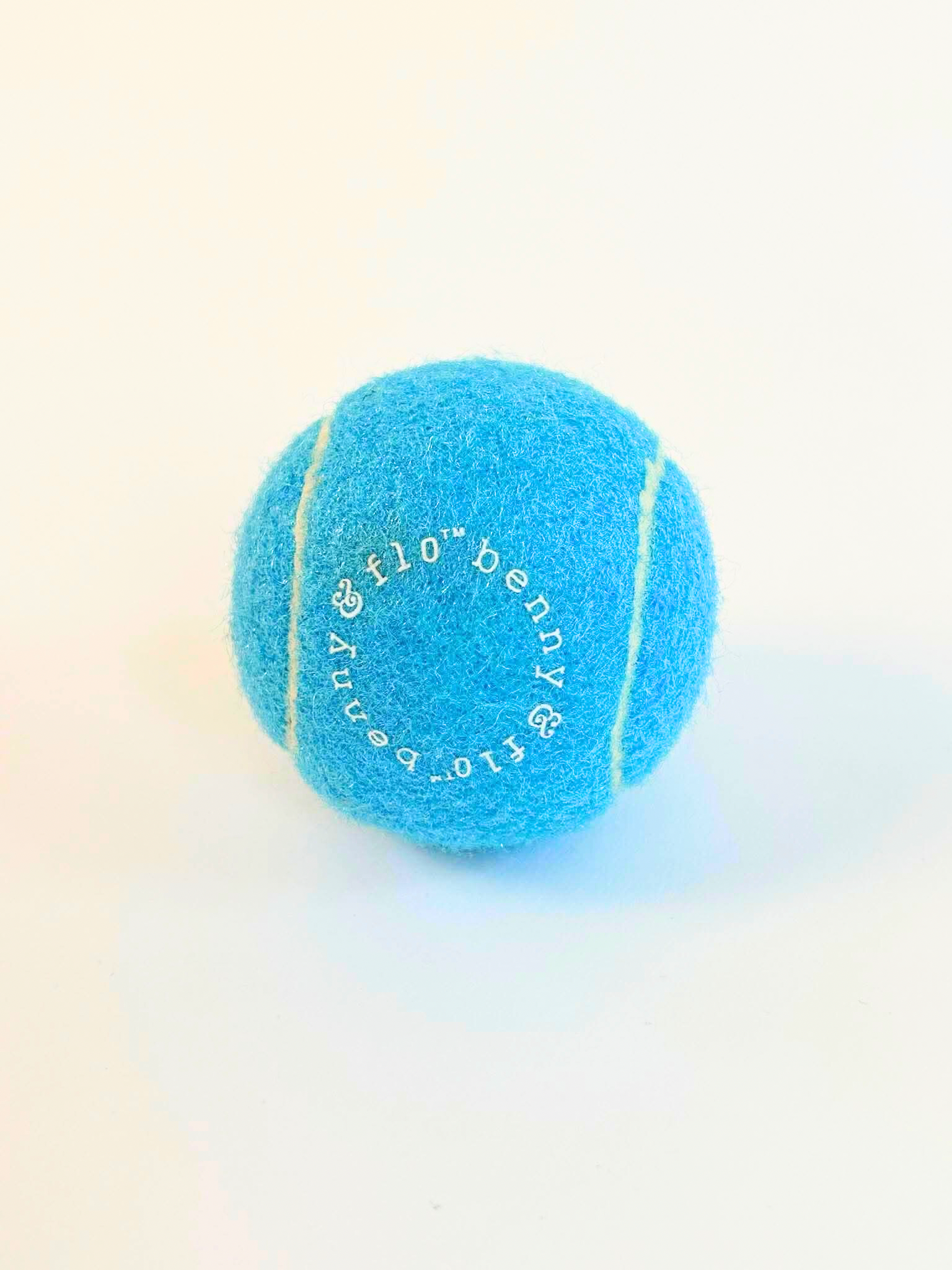 Blue tennis ball with 'benny & Flo’ branding on a light background