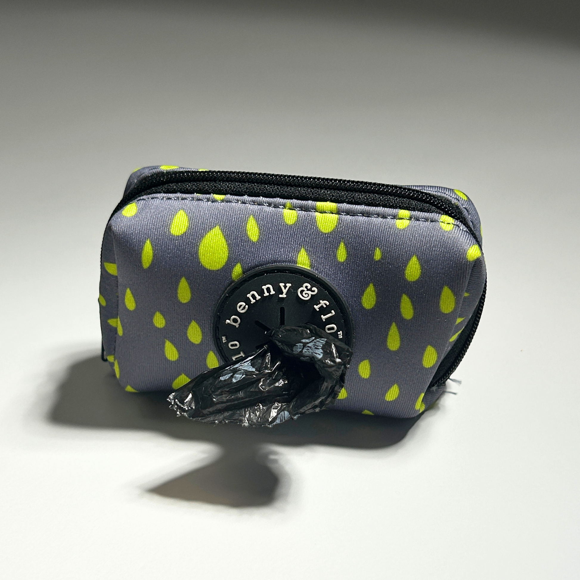 Grey poop bag holder with green raindrop pattern on a white background