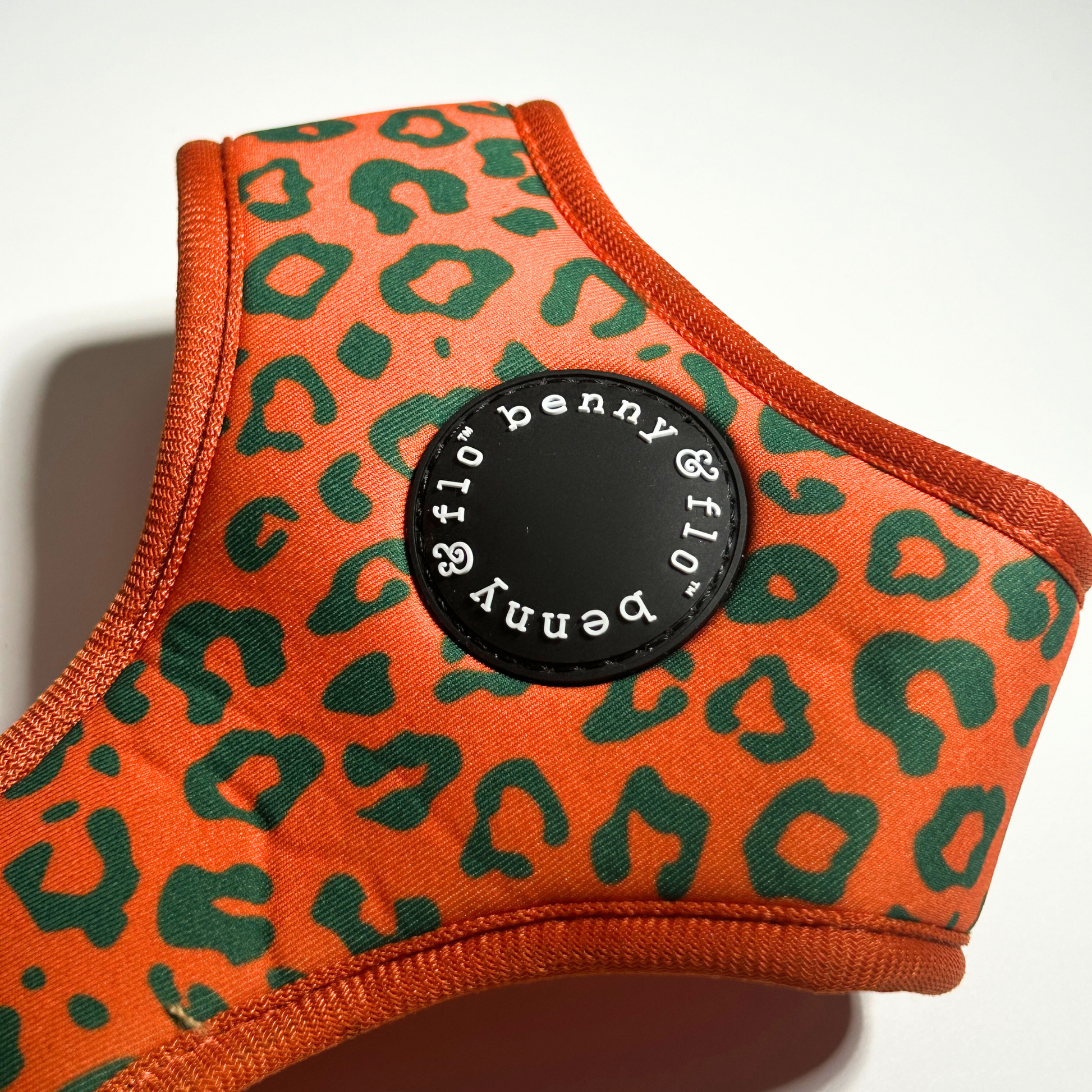 Orange and green patterned dog harness with a black label on a white background
