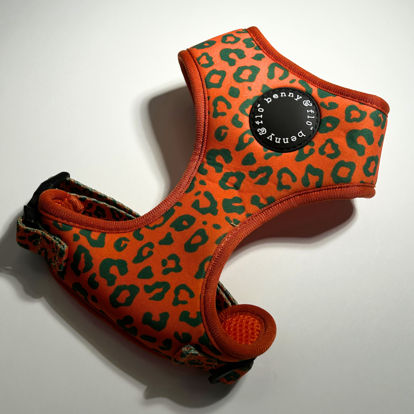 Orange and green leopard print dog harness with brand label on a white background