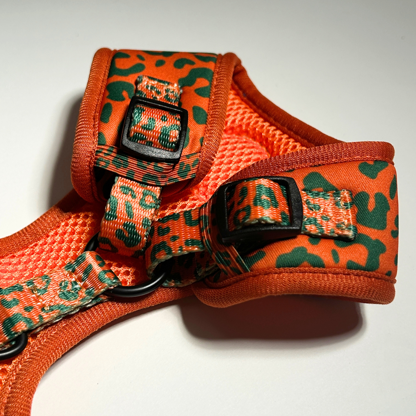 Orange and green patterned dog harness on a white background
