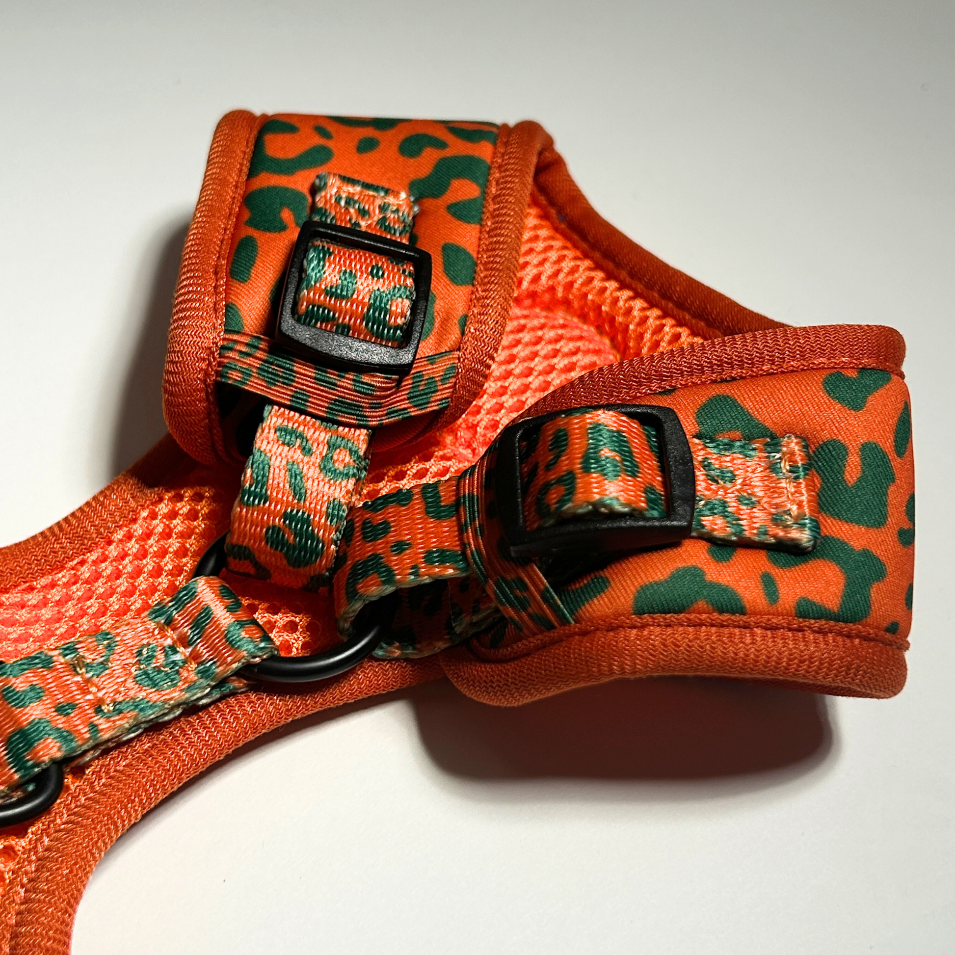 Orange and green patterned dog harness on a white background